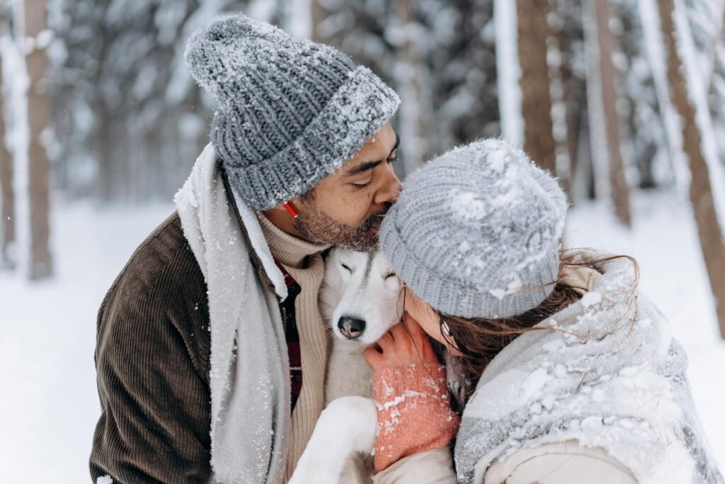 A romantic winter scene featuring a couple and a Siberian Husky sharing warmth and affection amidst a snowy backdrop.